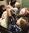 Flere barn står tett sammen og rekker hendene opp i et trangt innendørs rom.
