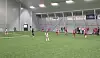 Fotballspillere i ulike drakter under kamp på kunstgress i en innendørshall.