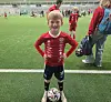 Ung fotballspiller i rød drakt står over en ball på en kunstgressbane.
