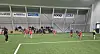 Unge fotballspillere spiller kamp på kunstgress i en innendørshall.