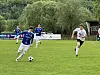 Fotballspiller i blå drakt fører ballen foran motspillere i hvitt på en gressbane.