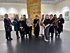 En gruppe mennesker poserer i et lyst galleri med kunst på veggene.