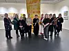 En gruppe mennesker poserer i et lyst galleri med kunst på veggene.