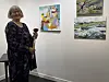 Kvinne i mønstret kjole står ved siden av tre kunstverk i et galleri.