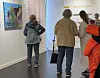 Besøkende/kunstnere betrakter kunstverk i et lyst galleri.
