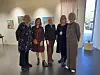 Fem voksne poserer i et lyst galleri med kunst på veggene.