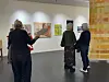 Noen mennesker i et lyst galleri med mest fargerike kunstverk.