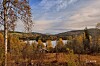 Høstskog, innsjø og liten hytte omgitt av åser under en skyet himmel.
