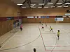 Håndballspillere i aksjon på en lys idrettshallbane med mål i venstre side.