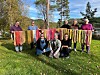 Gruppe personer viser fargerike håndlagde tekstiler utendørs i en park.