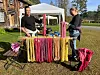 Utendørs bod med fargerikt garn, tekstiler og to personer i solskinn.