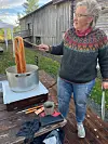 Kvinne håndterer oransje ullgarn i en metallgryte på en terrasse ved en trebygning.