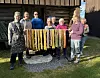 Gruppe mennesker med fargerike tekstiler foran en gammel trebygning.