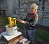 Kvinne arbeider med gult garn i en kjele på ei kokeplate utendørs.