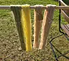 Fire buntede fibre i grønne, gule og brune nyanser henger på et gjerde utendørs.