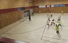 Håndballspillere i aksjon på en innendørs bane med tribune og trevegger.
