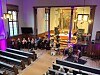 Et ensemble spiller konsert foran alteret i en opplyst kirke, mens publikum sitter i benkene.