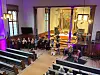 Et ensemble spiller konsert foran alteret i en opplyst kirke, mens publikum sitter i benkene.