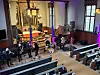 Musikere spiller foran alteret i en kirke, mens publikum sitter i benkeradene.