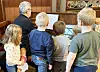 Gruppe besøkende samlet rundt en organist et trepanelkledd rom.