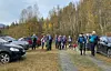 Turgruppe på en grusvei mellom biler i et høstfarget skoglandskap.