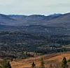 Fjell og skogkledde åser med høstfarger under en overskyet himmel.