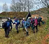 Turgåere med sekker og gåstaver ved ei gammel høyløe i høstfarget skog.