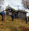 Vandrere utenfor en gammel trehytte i et høstlig landskap.