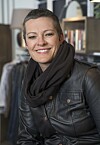 Smilende kvinne i svart skinnjakke og skjerf foran en bokhylle.