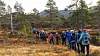 Turgåere med ryggsekker går på rekke gjennom en høstlig skog med fjell i bakgrunnen.