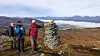 To turgåere ved en steinvarde i et åpent fjellandskap med innsjøer og fjell i bakgrunnen.