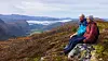To turgåere sitter på en fjellrygg med utsikt over fargerike fjell og daler.