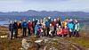 Turgåere samlet på en steinete fjellvidde med fjell i bakgrunnen.
