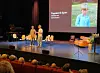 To personer på en scene foran et lerret med bilde av et barn.