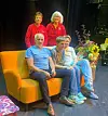 Fire personer samlet rundt en oransje sofa på en scene med blomster og planter.