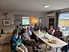Gruppe mennesker sitter samlet rundt bord med kaffe og mat i et lyst møterom.