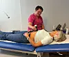 Behandler bruker et håndholdt apparat på en kvinne som ligger på en blå klinikkbenk.