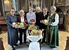 Ei gruppe voksne damer holder kurver med frukt, grønnsaker og blomster innendørs.