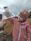 Barn i rosa klær holder en gjennomsiktig plastpose med vann og en liten fisk i, i et overskyet fjellandskap.