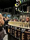 Gjester ved en bardisk med champagneglass og fargerik kunstinstallasjon i et moderne lokale.