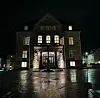 Opplyst historisk steinbygning ved en regnvåt plass om natten.