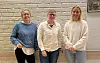 Tre kvinner i hverdagsklær står på rekke foran en lys murvegg.