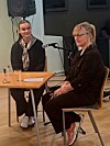 To kvinner sitter ved et bord med mikrofoner i et innendørs lokale.