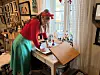 Kunstner i rødt og turkis arbeider med skisser ved et tegnebord i et atelier.