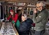 Tre personer vurderer bilder og grafiske arbeider ved et bord i et kunstverksted.