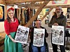 Tre voksne viser fram svart-hvite illustrasjoner i et verksted med kunst på veggene.