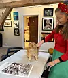 Kvinne klapper en katt på et bord i et rustikt rom med kunst på veggene.