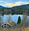 Liten hytte ved en speilblank innsjø omgitt av høstskog og åser.