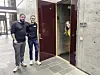 Tre personer ved en bygning med mørkerød inngangsdør og grå betongfasade.