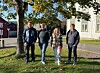 Fire personer står samlet på en gressplen foran et lyst trehus.